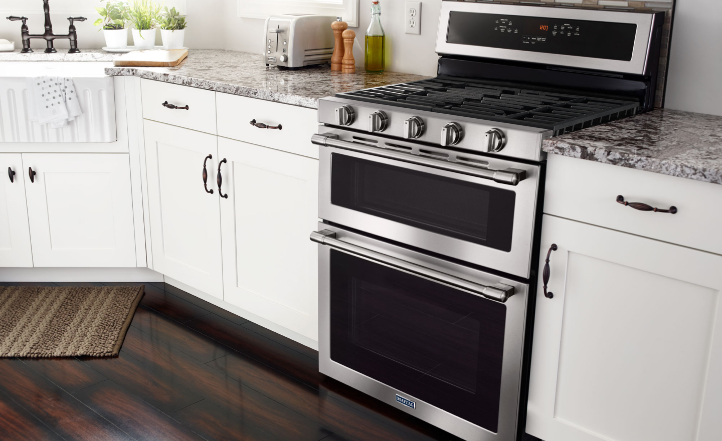 Stainless steel Maytag® gas range in kitchen between countertops and white cupboards