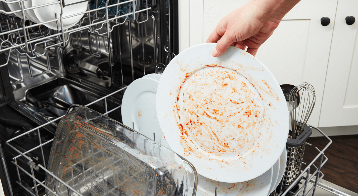Side view of open dishwasher with racked filled with plates, glasses and bowls
