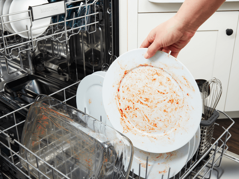 Side view of open dishwasher with racked filled with plates, glasses and bowls