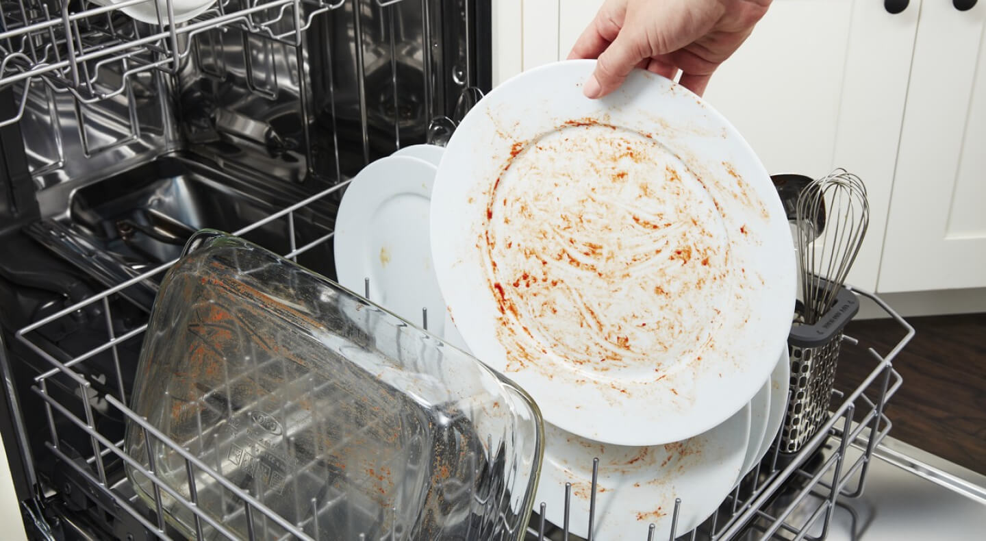 A person placing a dirty dish in a Maytag® dishwasher