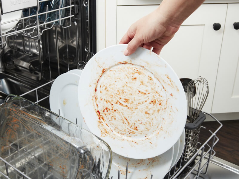A person placing a dirty dish in a Maytag® dishwasher