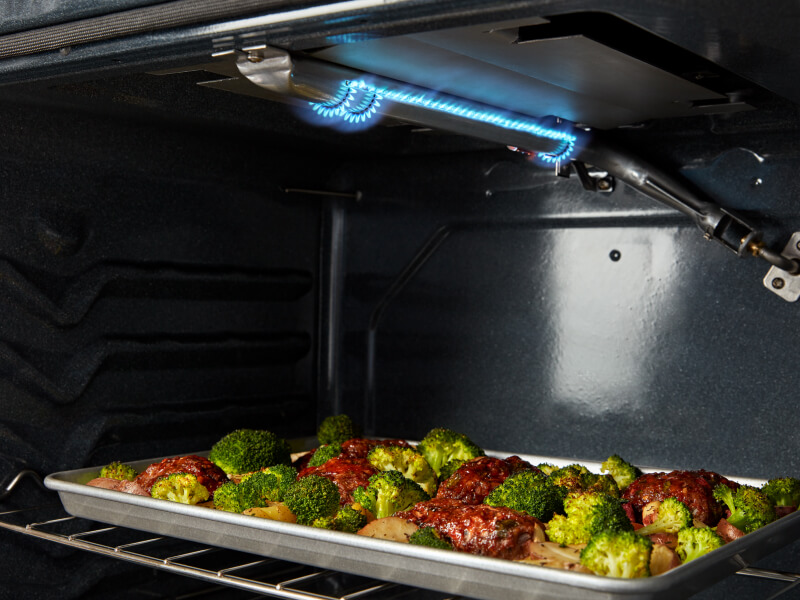 Blue flame on the roof of an oven cavity above roasting meat and vegetables