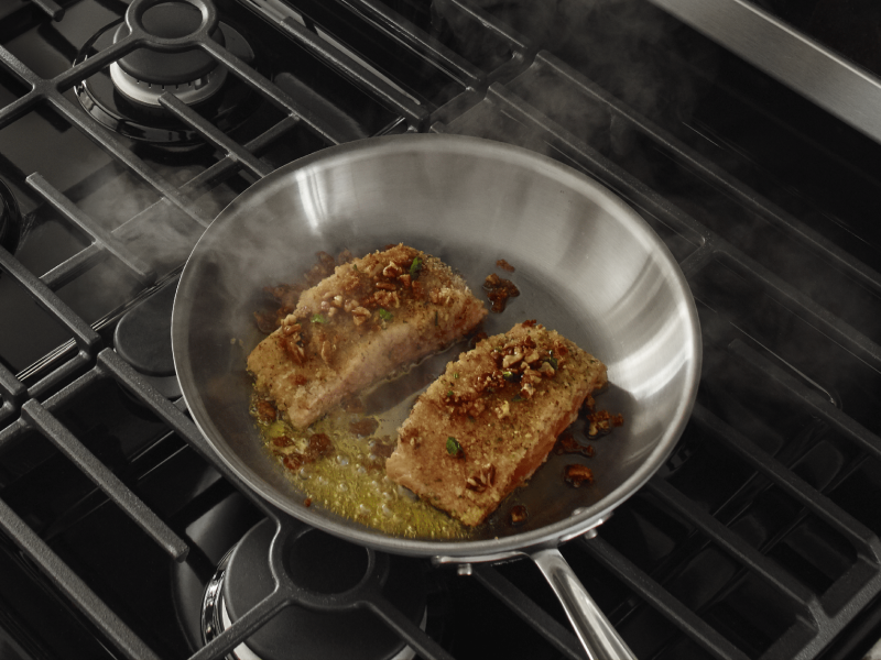 Fish filets simmering in a stainless steel pan with oil