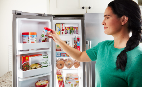 Person removing frozen food from a side-by-side fridge freezer compartment
