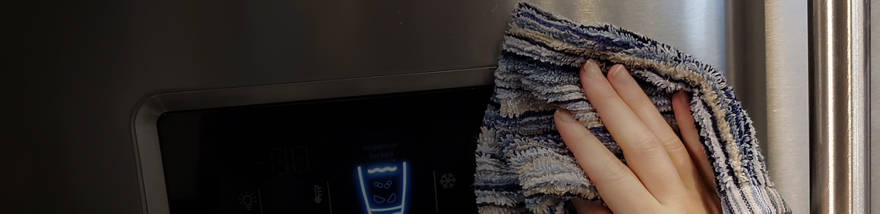 A hand cleaning the surface of a Maytag® refrigerator