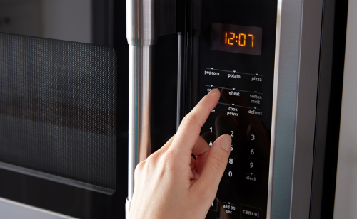Person selecting settings on a stainless steel, over-the-range microwave control panel