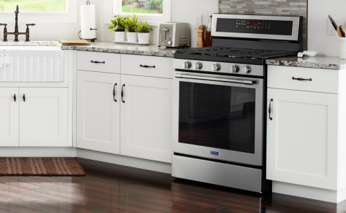 Maytag stainless steel oven set between white cabinets