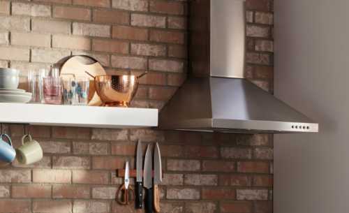 Stainless steel range hood on a brick kitchen wall
