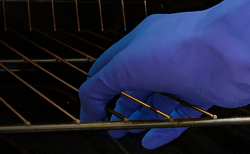Hand wearing blue glove removing oven rack from oven cavity