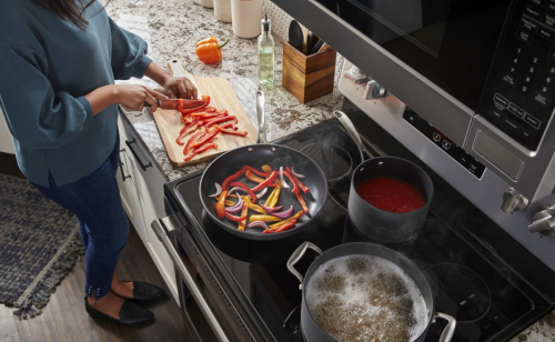 Woman chopping a red bell pepper on a wooden cutting board next to an electric range