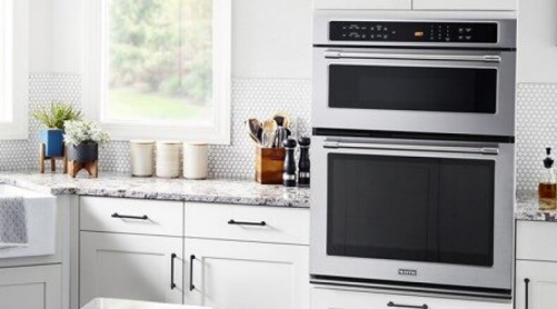 A Maytag® wall oven microwave combo placed between white cabinets with gray countertops