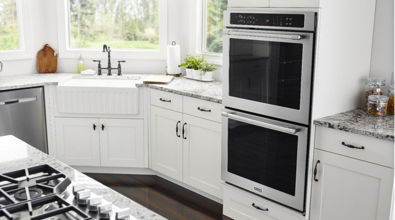 A Maytag® double wall oven place in a kitchen with white cabinets, gray marble countertops and white sink