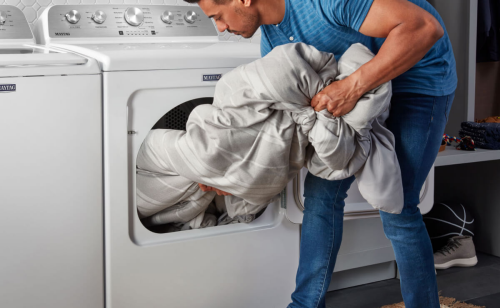 A person loading a comforter into a Maytag® front load dryer