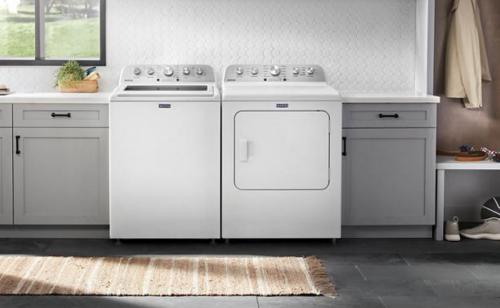 Overview of a laundry room with a top load washer, front load dryer, gray cabinets, and white backsplash tile.