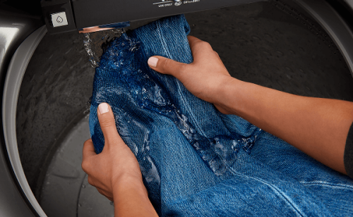 Person washing denim jeans under the built-in water faucet in a Maytag® washer