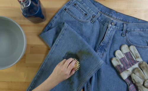 A hand scrubbing a grass stain on a pair of jeans