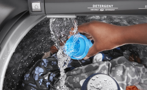 Someone rinsing a detergent cap in the water stream of their washer
