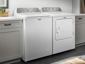 A white Maytag® top load washer and dryer next to grey cabinetry