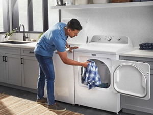 Person loading clothes into an open white Maytag® dryer