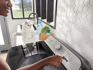 A woman starting her washer while a cat looks on