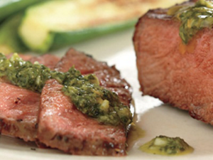 A close-up of slices of steak with a green sauce poured over them