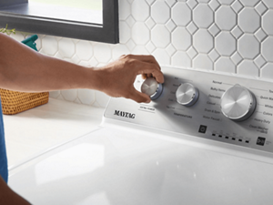 A hand turning a Maytag® washer dial to the Extra Power setting