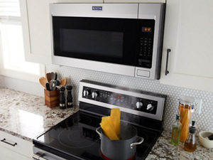 A Maytag® over-the-range microwave venting steam from a pot of pasta on a stovetop