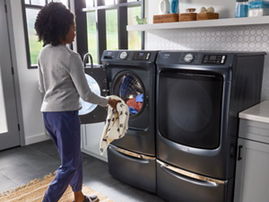 Person loading clothes into a gray, Maytag® front load washer on a pedestal